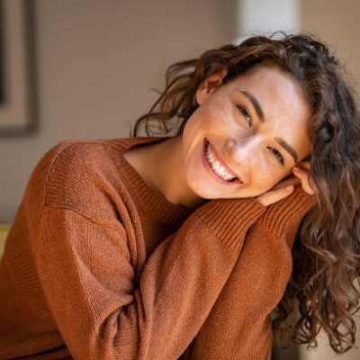 profile3 Happy young woman sitting on sofa at home and looking at camera. Portrait of comfortable woman in winter clothes relaxing on armchair. Portrait of beautiful girl smiling and relaxing during autumn.